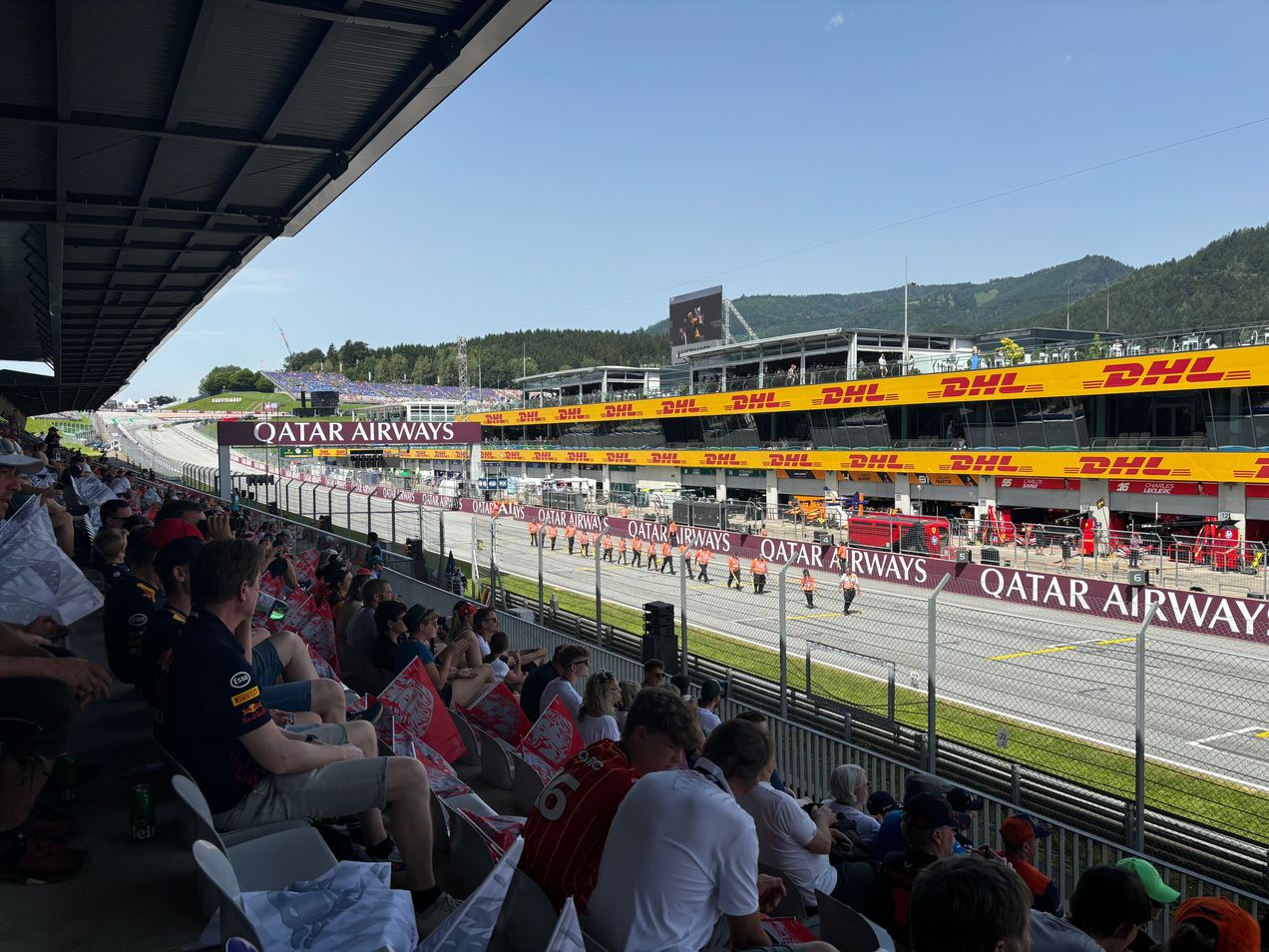 Fans op de hoofdtribune tijdens de GP van Oostenrijk terwijl stewards het startveld inspecteren