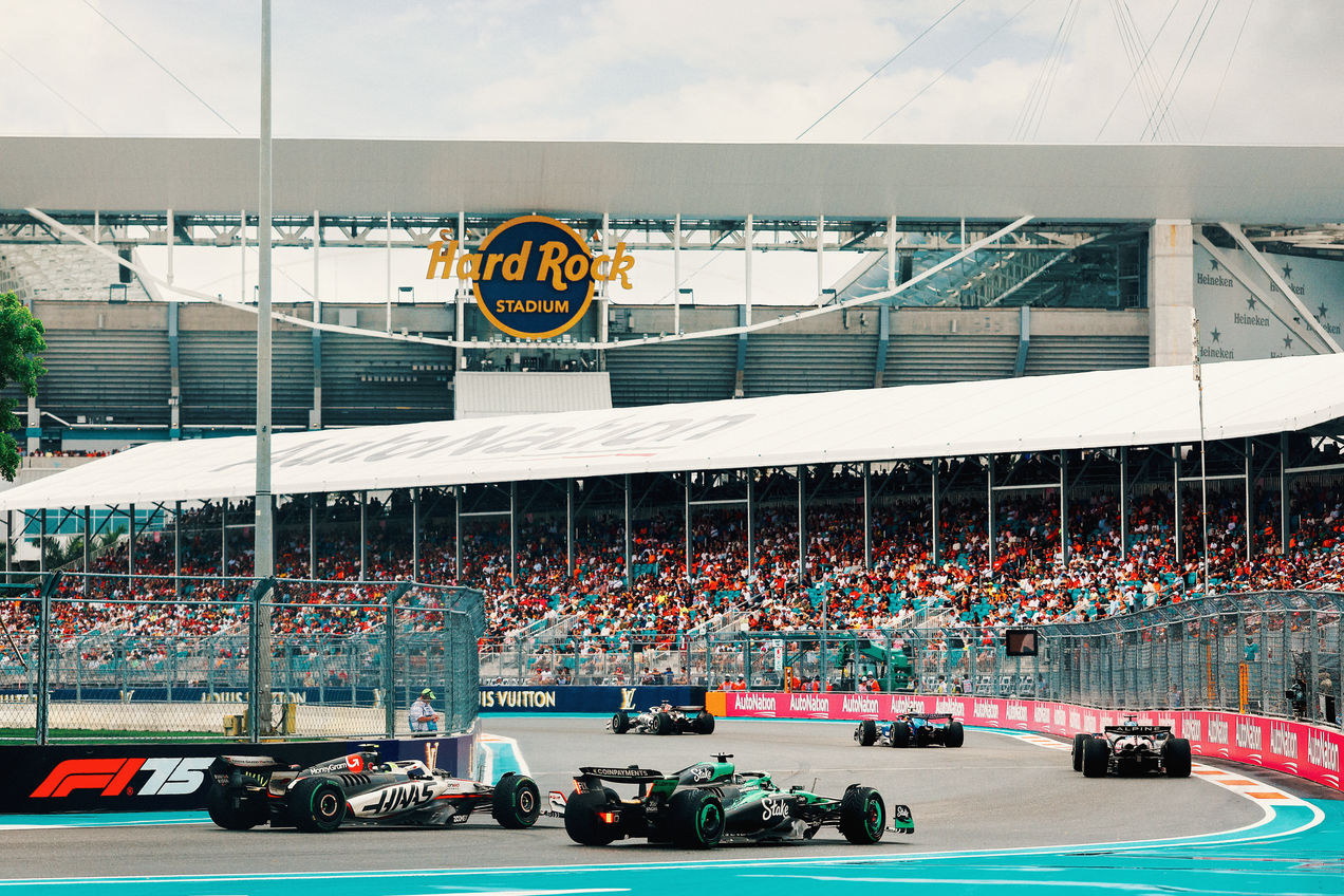 F1 cars race on the track of Miami with the Hard Rock Stadium in the background