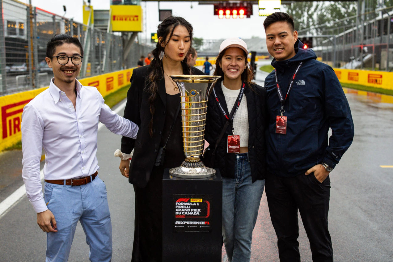 A group of fans stand around a Formula One trophy for a photo