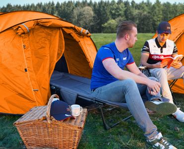 Two men sit in front of an orange tent at the camp grounds of the Belgium GP